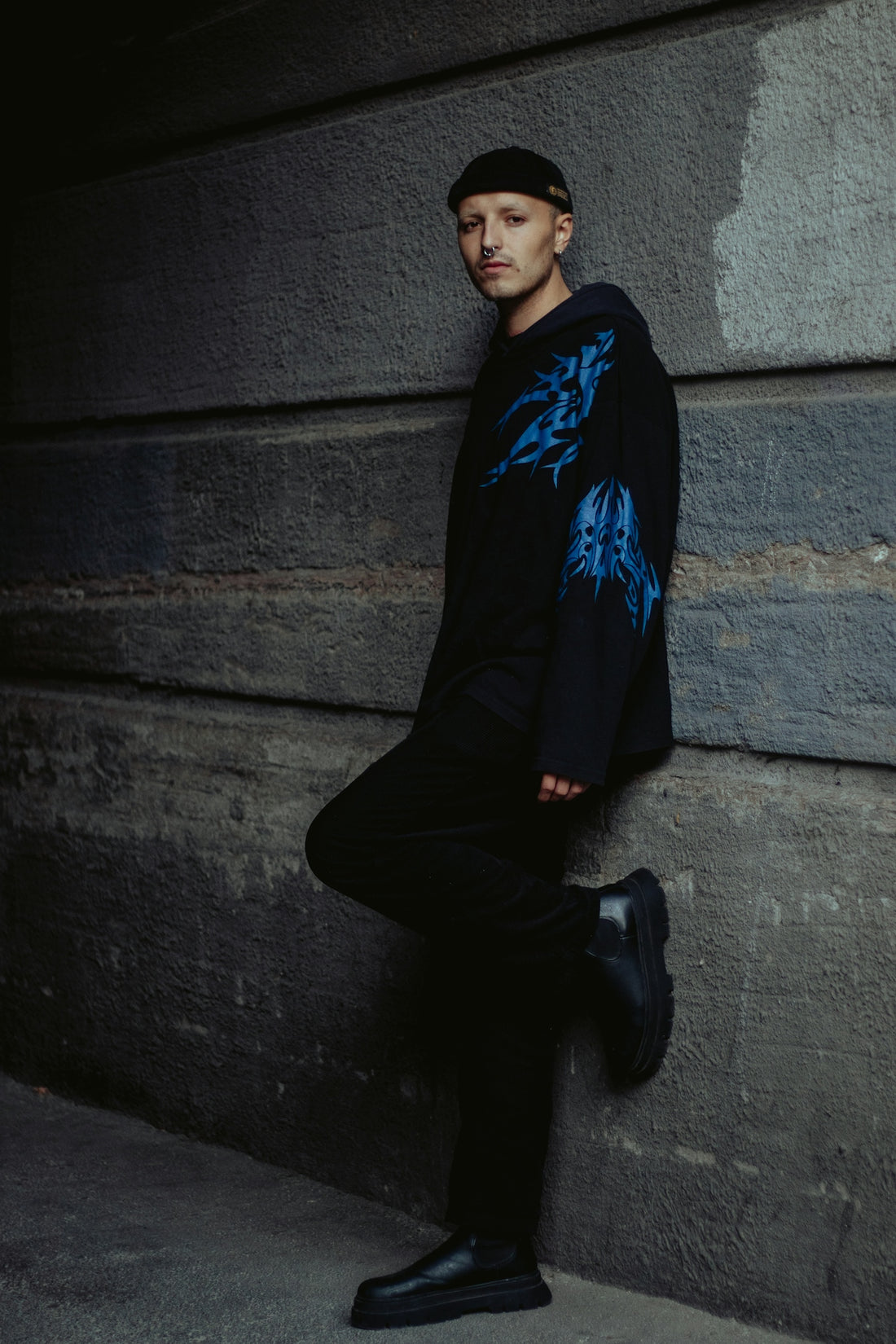 a man leaning against a wall wearing a black hoodie