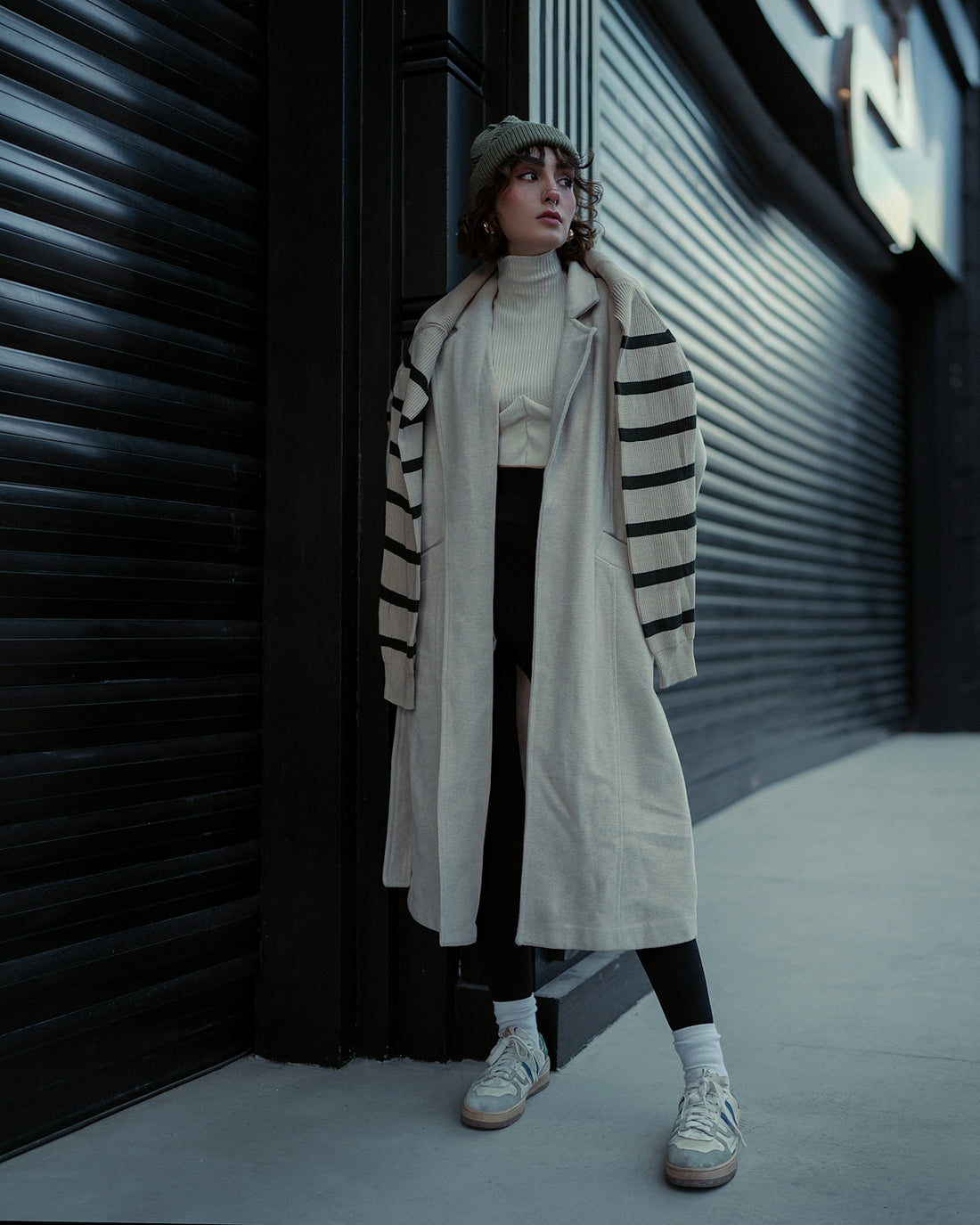 a woman leaning against a wall wearing a coat and hat