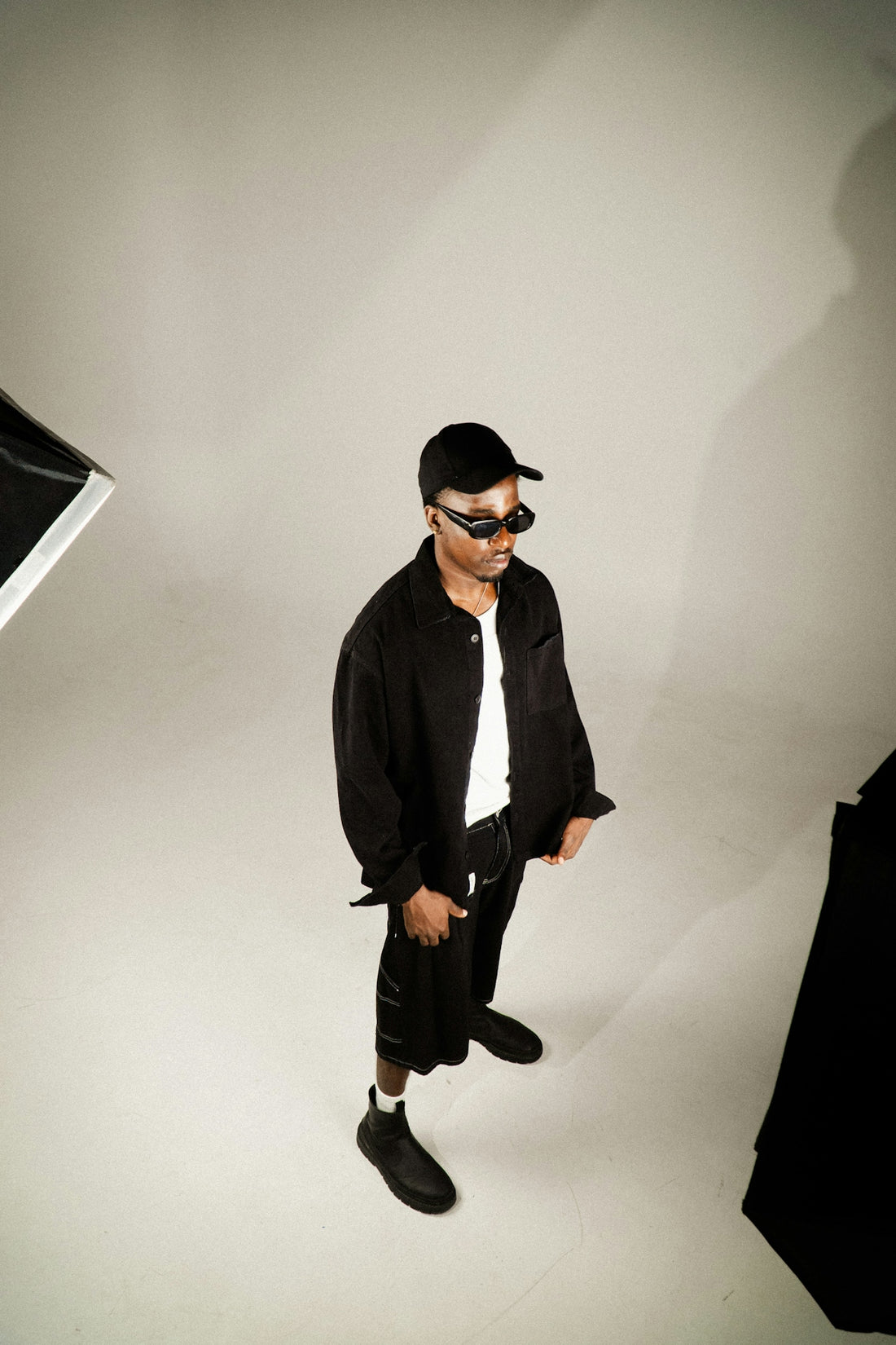 Man in black outfit and sunglasses posing in studio.